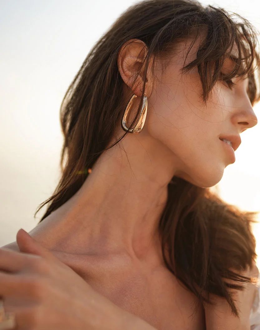 A close up of a woman with dark brown hair from the shoulders and up. She is wearing big gold earrings as she glances down away from camera. - Trapezius Barbie Botox in Fairfax, VA
